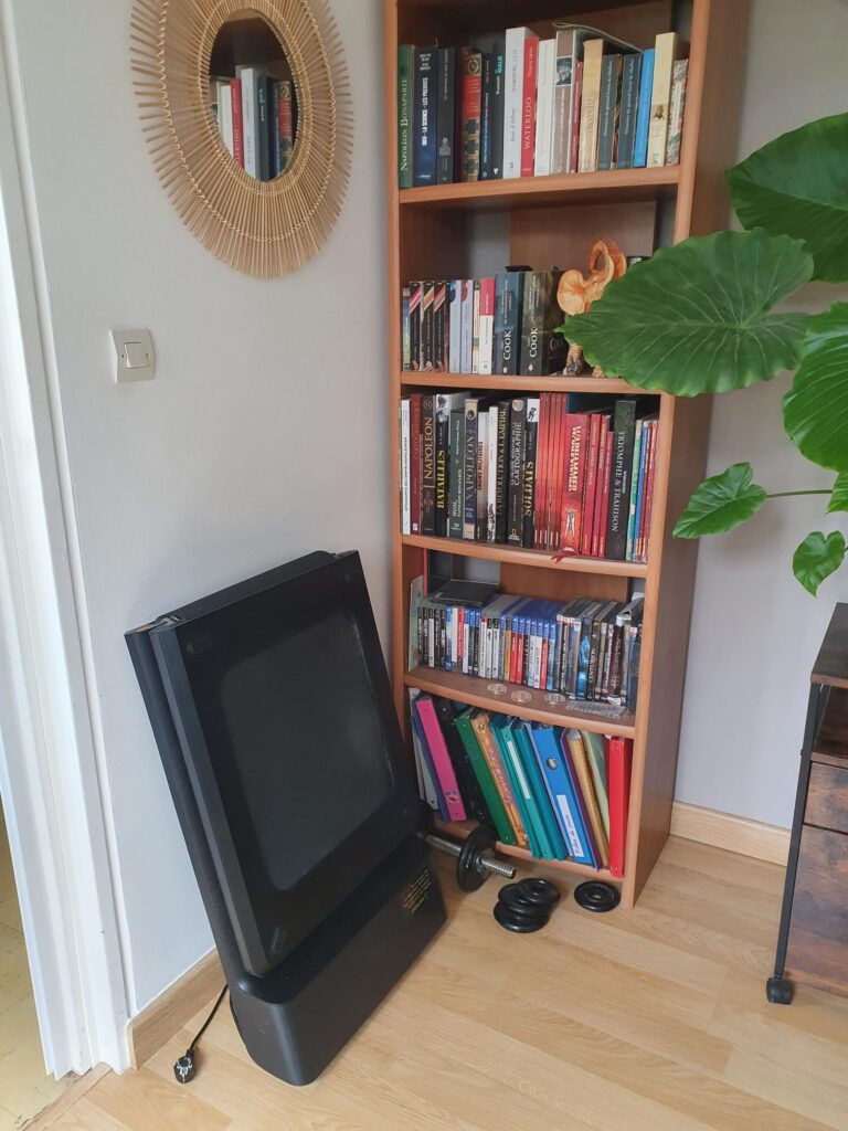 Un Walking Pad A1 pro plié et posé contre un mur, près d'une bibliothèque
